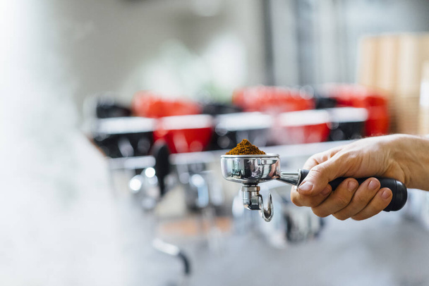 Λεπτομέρεια του ανθρώπου χέρι κρατώντας portafilter παραλήπτης γεμάτο με κόκκους καφέ κατά την προετοιμασία espresso - Φωτογραφία, εικόνα