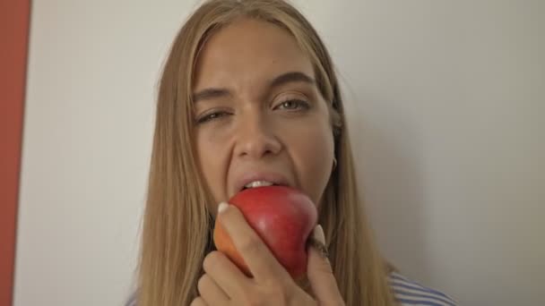 Una joven alegre está comiendo una manzana en la cocina de su casa
 - Metraje, vídeo