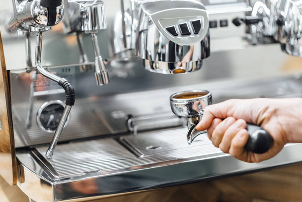 Foto ravvicinata del barista che trattiene il portafiltro mentre la macchina da caffè produce caffè espresso fresco in vetro - Foto, immagini