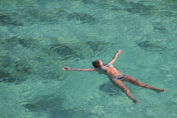 uma jovem deita-se de costas, de volta à superfície calma do tranquilo oceano azul-turquesa
. - Foto, Imagem