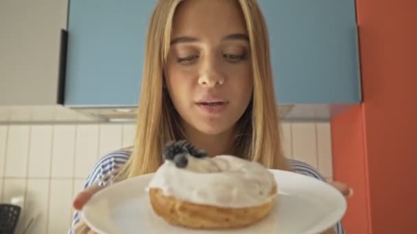Egy gyönyörű fiatal nő tortát tart a konyhában, és otthon érzi az illatát. - Felvétel, videó