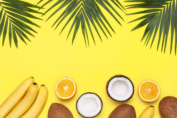 Summer tropical composition. Green tropical leaves of palm trees and monstera, coconut, orange, bananas on bright yellow background. Flat lay, top view, copy space. Creative background food, fruit. - Photo, Image