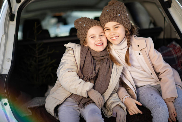 Two sisters sitting in the trunk of a car and hug - Fotoğraf, Görsel