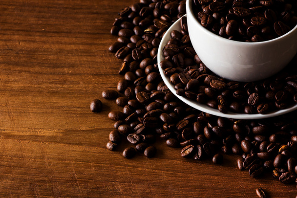 Roasted coffee beans in white cup on wooden background - Fotó, kép