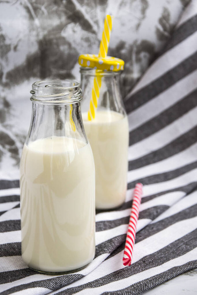Garrafa de leite fresco na mesa, garrafa de leite retrô com palha listrada e mais garrafa
 - Foto, Imagem