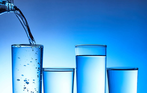Water in glas gieten op blauwe ondergrond - Foto, afbeelding