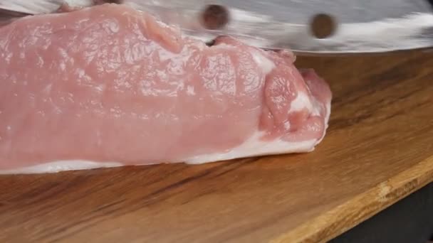 Close-up zicht op de vrouwelijke handen van een kok gesneden verse stukken varkensvlees op een houten keukenbord in rustieke stijl met een groot keukenmes - Video