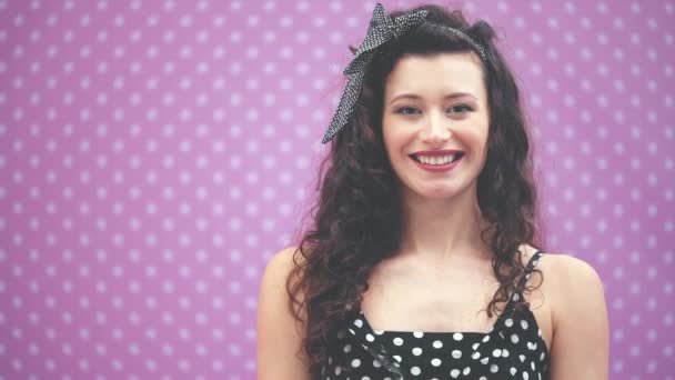 Pretty young lady with curly black hair and headband in polka-dots, showing a bar of chocolate to the camera. Blurred forefront. - Filmati, video
