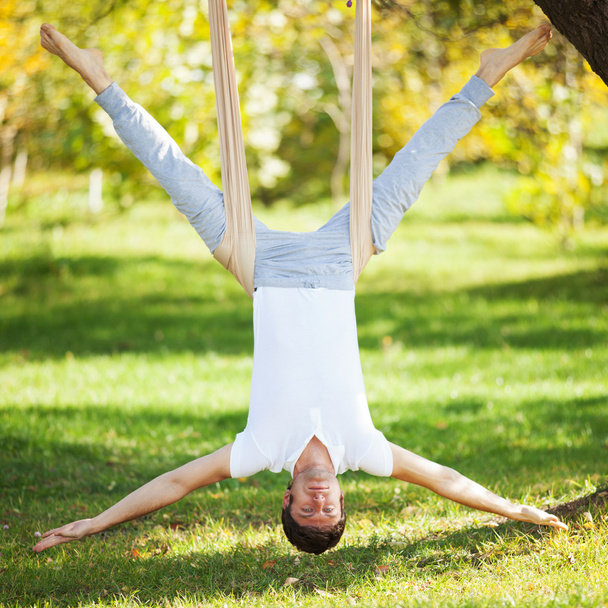 Anti-gravity Yoga, man doing yoga exercises in the park - Fotó, kép
