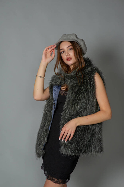 magnificent portrait of a beautiful young woman. Perfect face beautiful girl portrait. brunette girl. Girl in a gray hat. little black dress. Girl in a vest with faux fur. - Zdjęcie, obraz