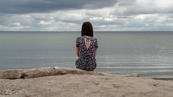 A lonely girl in a dress sits on the shore. - Photo, image