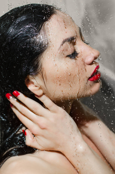 Close-up portrait of beautiful woman in shower. Model under shower closed her eyes with bright lips. Wet model with drops of water on face - Foto, Imagen