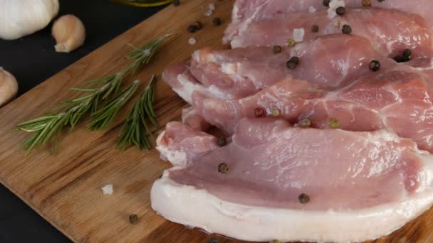Friss, nagy rózsaszín szalonnahús húsdarabok az otthoni főzés vágódeszkáján, rusztikus stílusban, fekete és vörös borssal és durva sóval díszítve - Felvétel, videó
