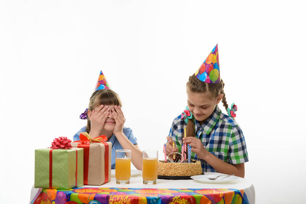 Uma menina coloca velas em um bolo de aniversário, o outro fechou os olhos
 - Foto, Imagem