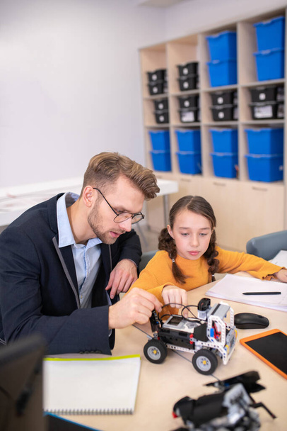 Male teacher and girl sitting at desk, studying buildable car - Foto, Bild