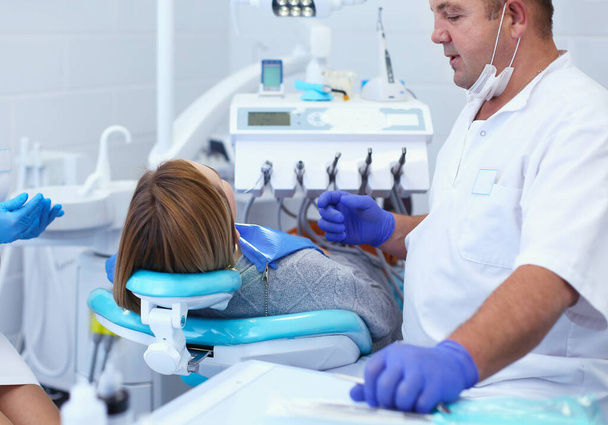 Старший стоматолог мужского пола в стоматологическом кабинете беседует с пациенткой и готовится к лечению - Фото, изображение