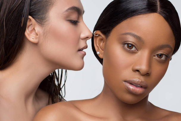 Schönheitsporträt von Afrikanerinnen und Europäerinnen mit nackten Schultern und modischem Make-up stehen dicht beieinander auf weißem Hintergrund. zwei schöne Mädchen unterschiedlicher Rassen dunkelhäutig und weiß geschminkt - Foto, Bild