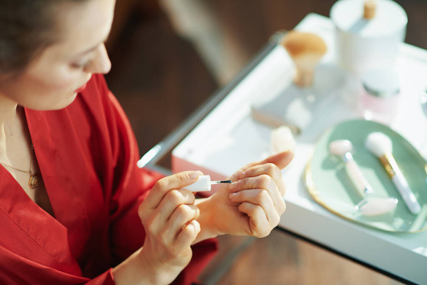 Closeup on housewife applying nail polish near table with toiletries at home in sunny day. - Valokuva, kuva