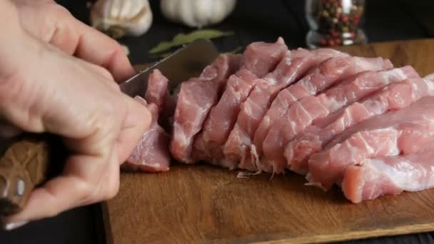料理人の女性の手は大きなキッチンナイフで素朴なスタイルで木製のキッチンボード上の豚肉ベーコン肉の新鮮な作品をカット - 映像、動画