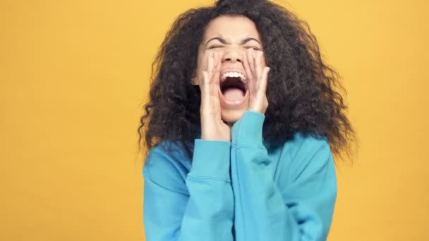 Close up portrait of young afro american woman shouting and looking at the camera. Yellow background. - Filmagem, Vídeo
