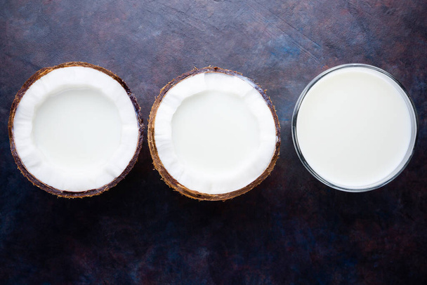 Kokosmilch und Kokosnuss in Glas auf dunklem Hintergrund. Kokos vegane Milch ohne Molkereiprodukte mit Kopierraum. Gesundes Getränk. Alternative Milch. Flache Lage - Foto, Bild