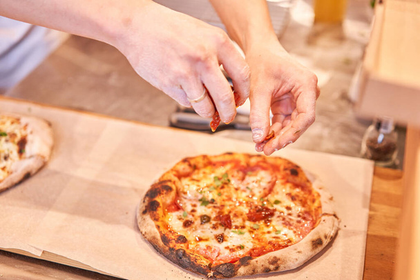 Chief adds ingredients on pizza to pieces at Neapolitan pizzeria. Italian kitchen and cooking concept. - Photo, Image