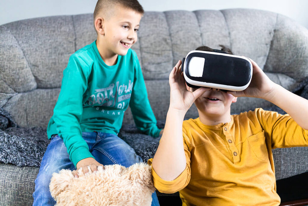 Cute, little boy having fun with vr headset with his brother next to him and teddy bear toy. Kids and technology concept - Foto, Bild