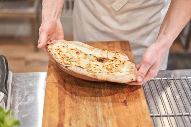 Olasz konyha és főzés koncepció. A főnök pizzavágóval darabokra vágja a pizzát a nápolyi pizzériában.. - Fotó, kép