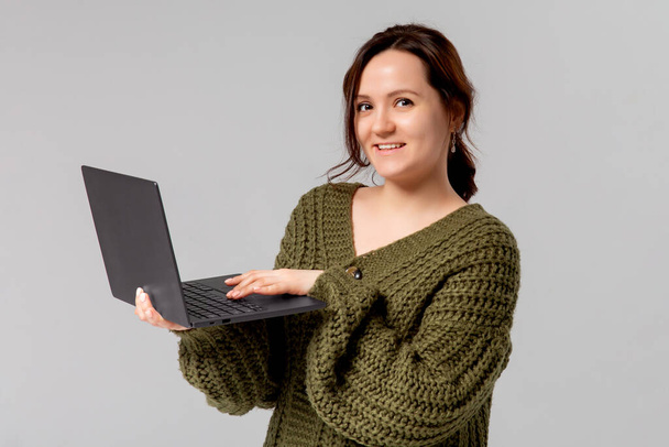 Γοητευτική νεαρή γυναίκα που εργάζονται freelance, απομακρυσμένο από το γραφείο, κρατήστε το laptop, δακτυλογράφηση πανεπιστήμιο έκθεση, στρίψτε αριστερά χαμογελώντας χώρο αντίγραφο, σταθεί γκρι φόντο χαρούμενη, περιήγηση web χρησιμοποιώντας υπολογιστή - Φωτογραφία, εικόνα