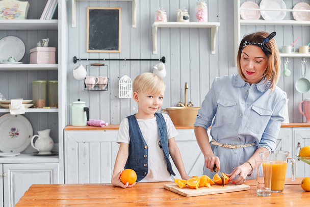 Comida saudável, fruta fresca, laranjas suculentas. Mãe e filho estão sorrindo enquanto tomam um café da manhã na cozinha. Manhã brilhante na cozinha
. - Foto, Imagem