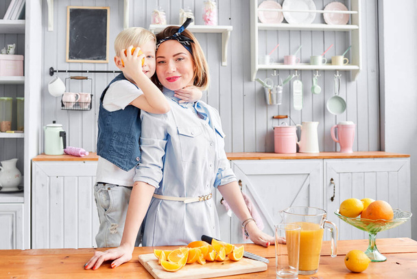 Egészséges étel, friss gyümölcs, lédús narancs. Anya és fia mosolyognak, miközben a konyhában reggeliznek. Jó reggelt a konyhában.. - Fotó, kép