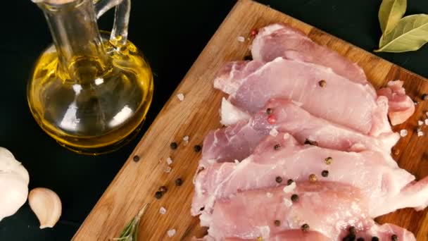 Verse plakjes varkensvlees op een houten keukenbord in rustieke stijl. Knoflook, rozemarijn, grof zout, peper, olijfolie. Huisgemaakt koken. - Video