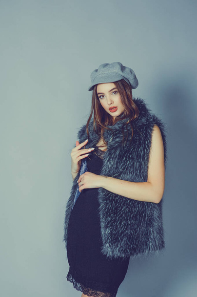 magnificent portrait of a beautiful young woman. Perfect face beautiful girl portrait. brunette girl. Girl in a gray hat. little black dress. Girl in a vest with faux fur. - 写真・画像