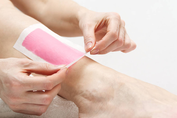 Žena s růžovými voskovými proužky. Krásná žena dělá depilaci pro její nohy s voskování, izolované na bílém - Fotografie, Obrázek