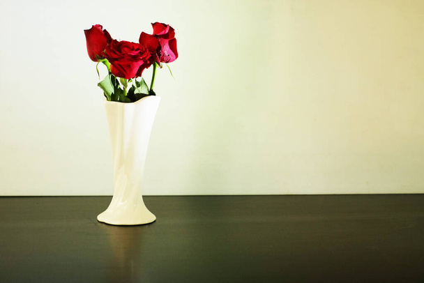 Kolme punaista ruusua klassisessa maljakossa valkoisella taustalla
 - Valokuva, kuva