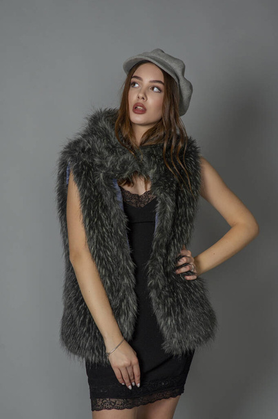 magnificent portrait of a beautiful young woman. Perfect face beautiful girl portrait. brunette girl. Girl in a gray hat. little black dress. Girl in a vest with faux fur. - Foto, Imagen