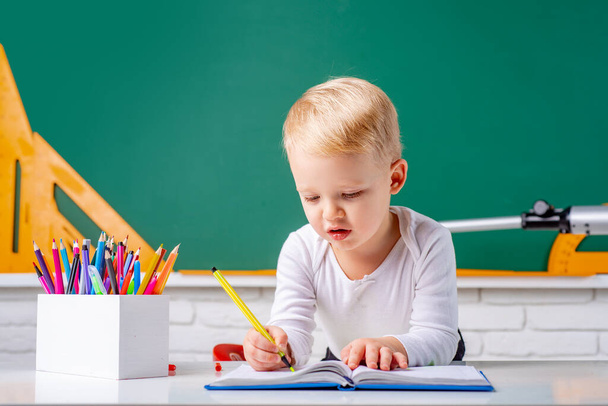Cute child boy in classroom near blackboard desk. Chalkboard copy space. Educational process. - Zdjęcie, obraz
