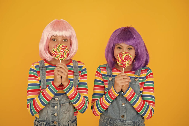 Sugary food to keep for yourselves. Small children hold lollipops yellow background. Little girls enjoy unhealthy food. Food or treats. Confections and candies. Food rich in sugar and carbohydrates - Foto, Imagen