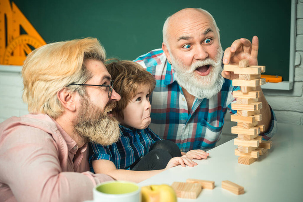 Grand-parent riant avec fils et petit-enfant relaxant passer week-end à la maison. Heureux famille homme amusez-vous ensemble et jouer Jenga
. - Photo, image