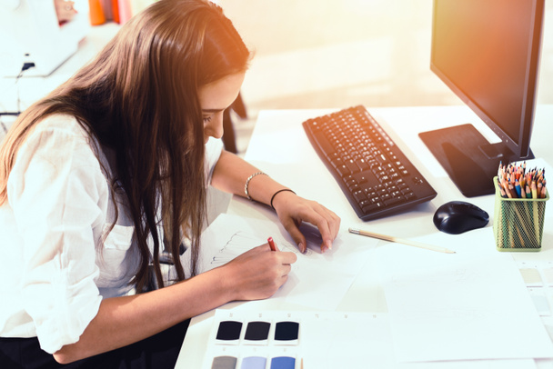 Muotisuunnittelija piirtää tai suunnitella vaatteita pöydälle mittaus tekstiili materiaali sakset leikkaus kangas nuori nainen suunnittelija tyylikäs näyttelytila / suunnittelija työskentelee tietokoneen PC
 - Valokuva, kuva
