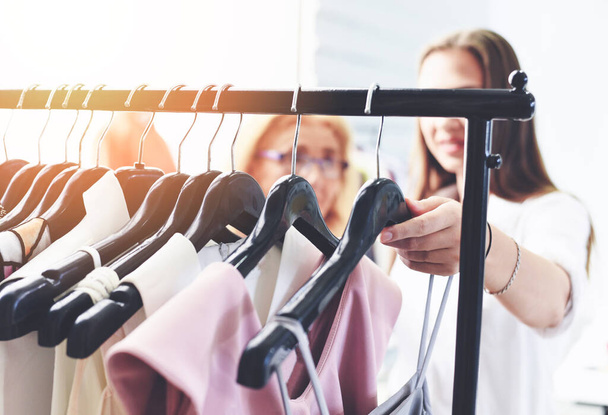 Ropa de moda de mujer de diferentes colores ropa en perchas en la sala de exposición / Compras mujeres eligen comprar ropa colgando ropa armario rack
 - Foto, Imagen