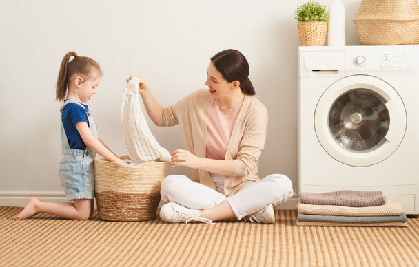Güzel genç kadın ve kız çocuk küçük yardımcı evde çamaşır yıkarken eğleniyor ve gülümsüyor..                                 - Fotoğraf, Görsel