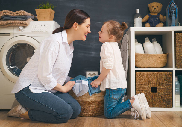 Gyönyörű fiatal nő és gyermek lány kis segítő szórakoznak és mosolyognak miközben otthon mosnak..                                 - Fotó, kép