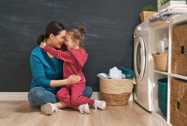 Beautiful young woman and child girl little helper are having fun and smiling while doing laundry at home.                                 - Foto, Imagem