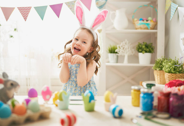 Beautiful child painting eggs. Happy family preparing for Easter. Cute little girl is wearing bunny ears.                                   - Fotó, kép