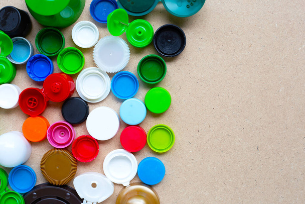 Tapas de botellas de plástico coloridas y tapa de vidrio de plástico sobre fondo de madera contrachapada. Vista superior
 - Foto, Imagen
