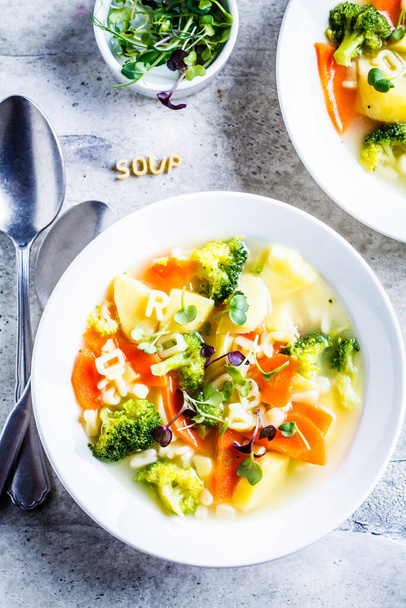 Zdravé děti abecední polévka se zeleninou a nudlovými písmeny v bílých talířích. Dětská výživa koncept. - Fotografie, Obrázek