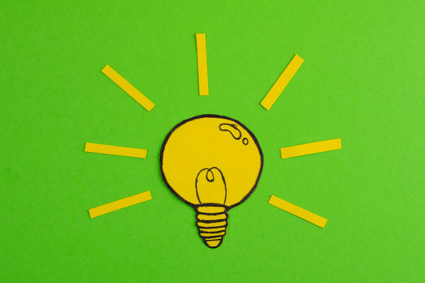 切り紙で構成され、緑の背景に電球を描きます。アイデアを象徴する創造的なコンセプト. - 写真・画像