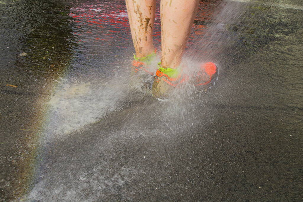 Runner washing mud from legs with sprinkler after the race on muddy terrain in Devon, UK - Photo, image
