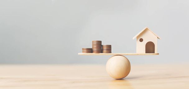 Drewniany dom i pieniądze monety stos na skalę drewna. Koncepcja inwestycji w nieruchomości mieszkalne i finansowe nieruchomości hipoteczne - Zdjęcie, obraz
